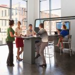 Image of group working at hightop long workspace wiht tv at one end.