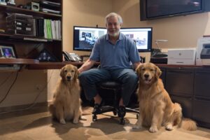 Image depicts founder of Alliance Corporate Services, Steve Bass seated in his home office with his two golden retrievers